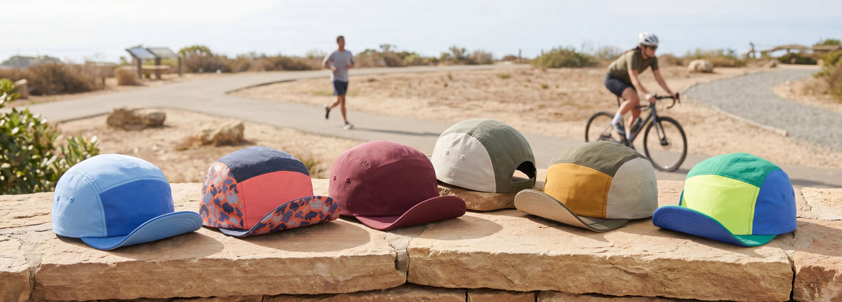 Colorful bike caps displayed on a stone ledge with people running and cycling in the background.