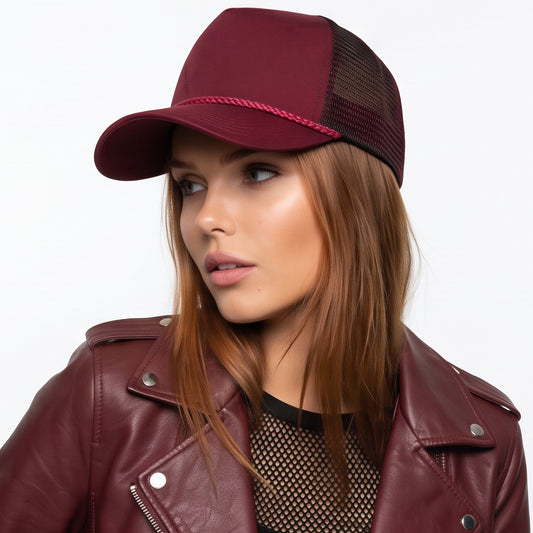 Woman wearing a maroon trucker cord baseball cap and leather jacket on a white background