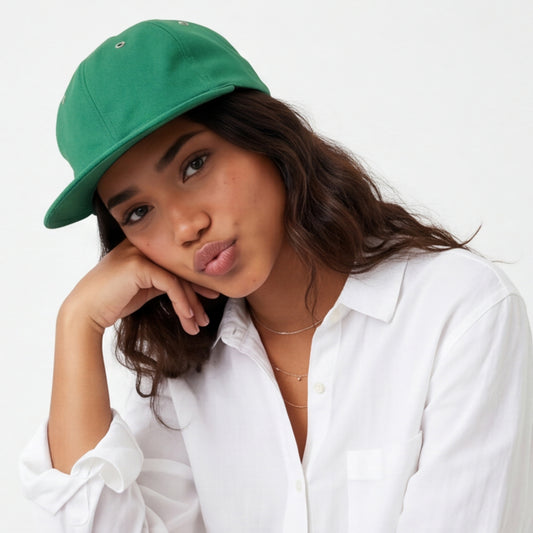 Woman wearing a green dad hat flat visor cap and white shirt against a white background