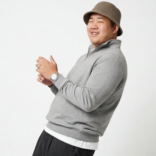 Person wearing a gray quarter zip sweat sweater and brown hat on a white background