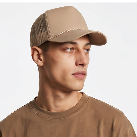 Man wearing a beige trucker cap with cord and matching shirt on a light gray background