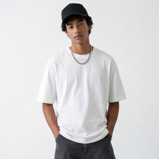 Person wearing a white oversized t-shirt, black cap, and dark pants on a plain background