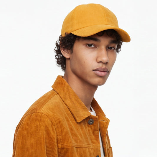 Person wearing a mustard yellow corduroy dad cap and jacket on a white background